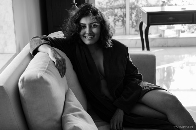 Nivedita Pohankar sitting on a sofa smiling at the camera with her hair blowing.