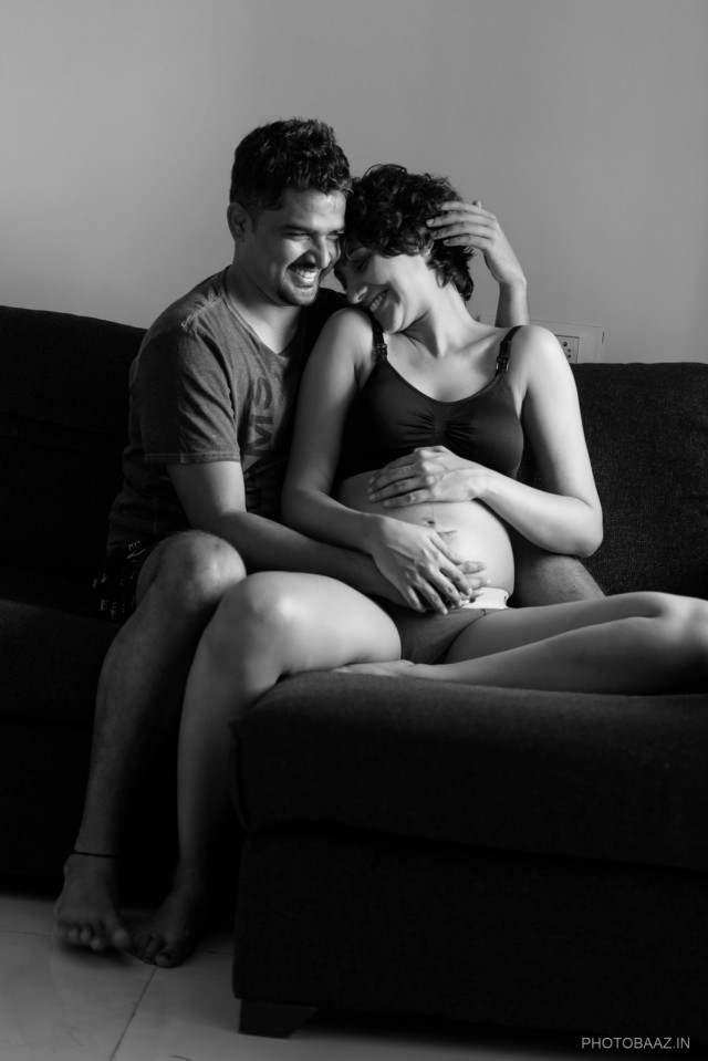 Couple in love sitting on a couch holding the woman's pregnant belly.